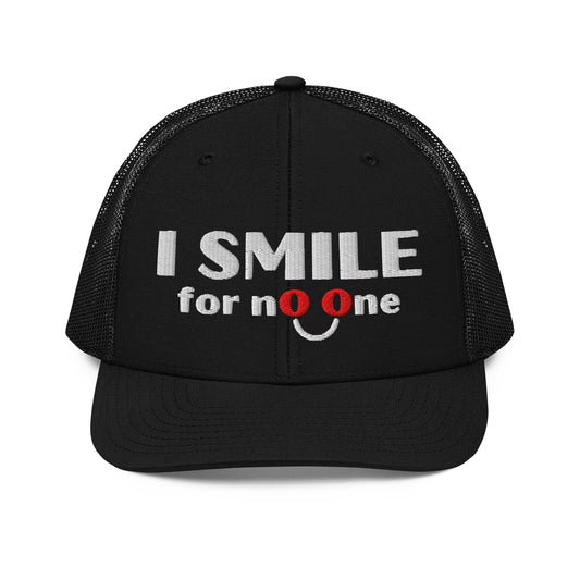 Black trucker hat with embroidered text 'I Smile for No One' in bold white lettering. Structured cap with mesh back and adjustable snapback.