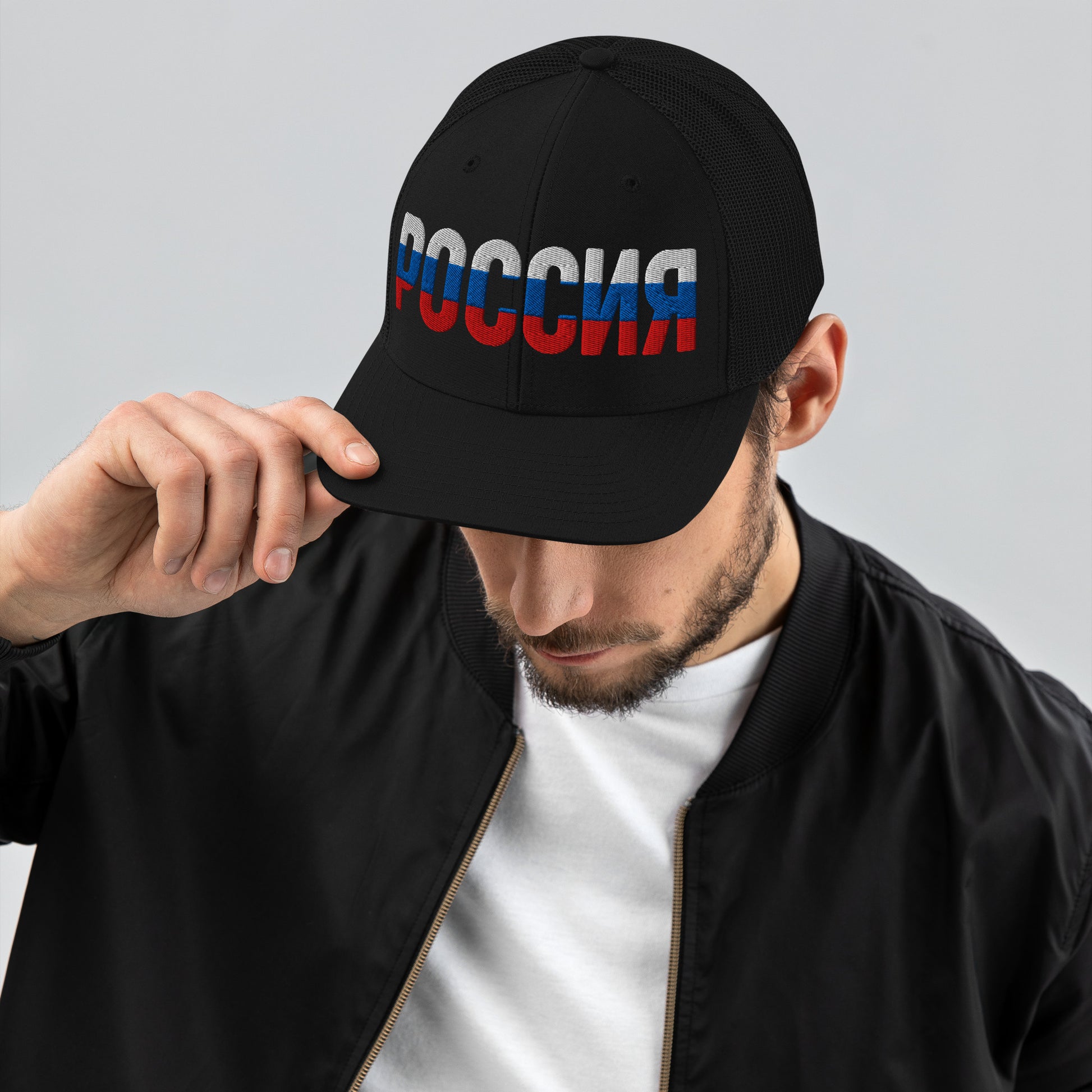 Man wearing a black trucker hat with “ROSSIA” embroidered in Russian flag colors (white, blue, and red).