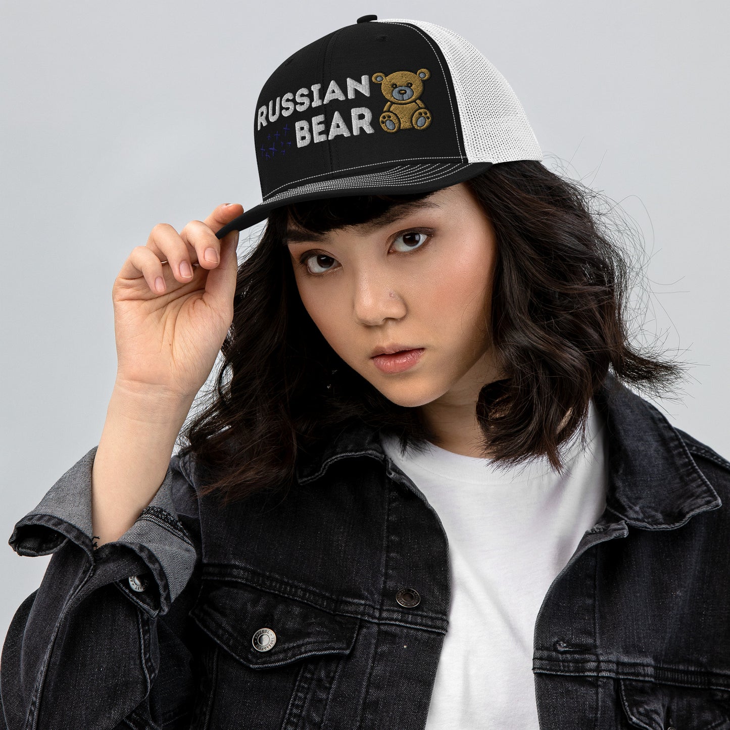 Woman wearing an embroidered trucker hat with 'RUSSIAN BEAR' text and cute bear design, featuring a structured front, white mesh back, and adjustable snapback closure.