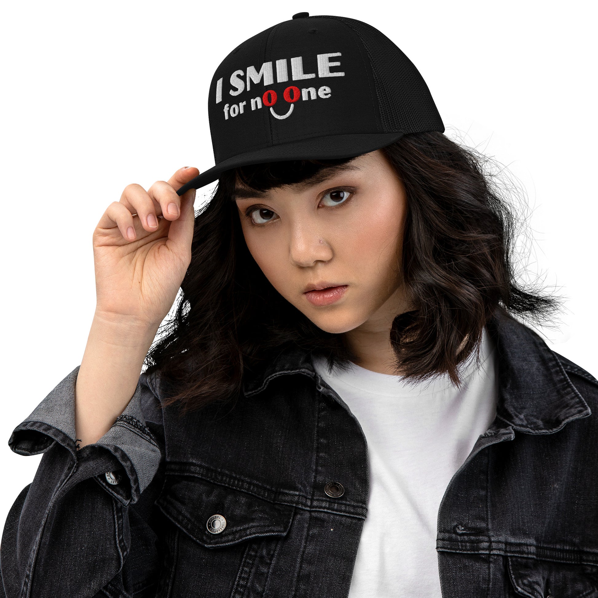Woman in a black trucker hat with embroidered text 'I Smile for No One' in bold white lettering. Structured cap with mesh back and adjustable snapback.