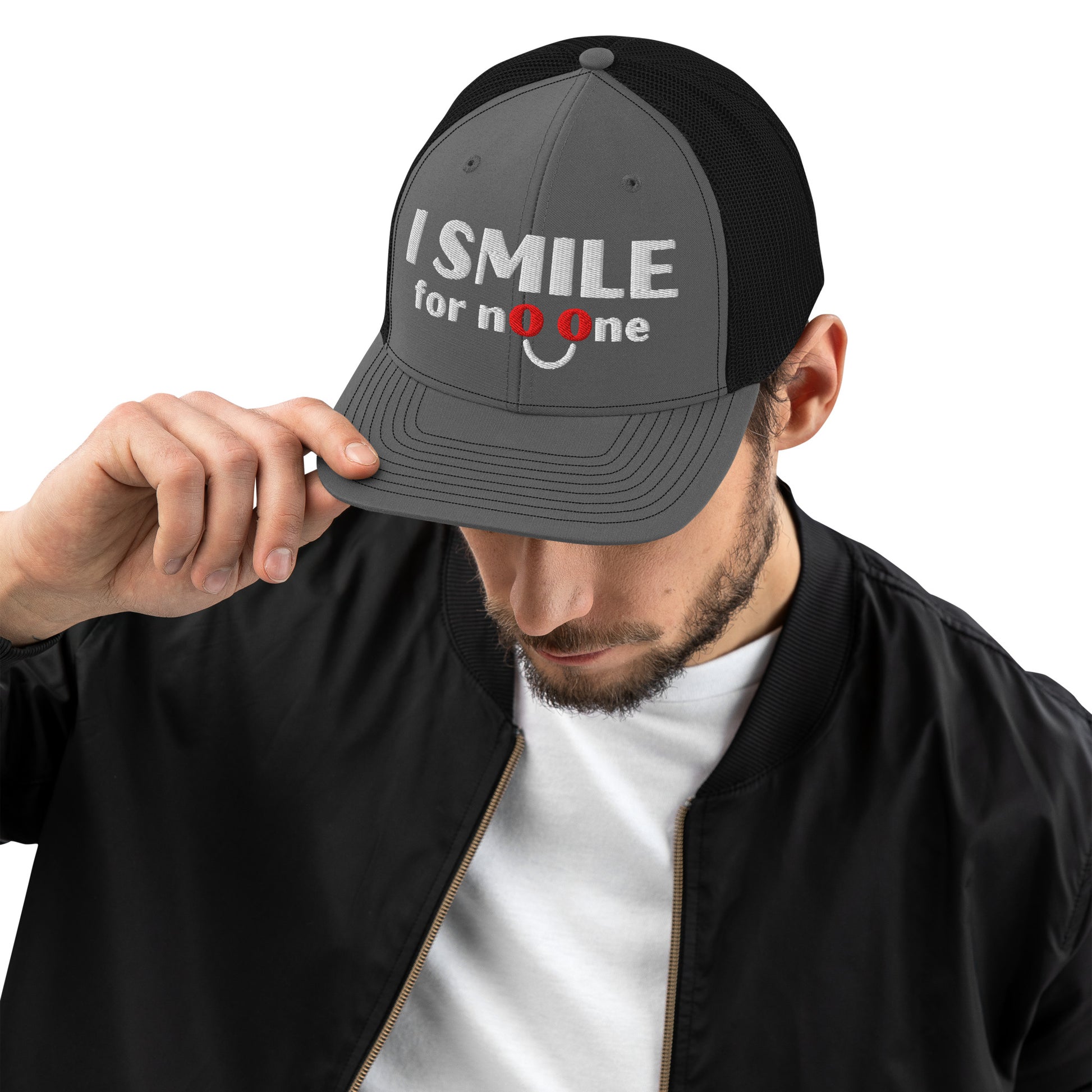 Man in a grey and black trucker hat with embroidered text 'I Smile for No One' in bold white lettering. Structured cap with mesh back and adjustable snapback.