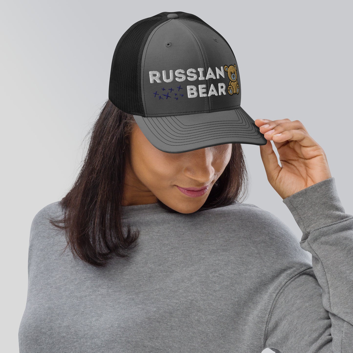 Woman wearing an embroidered trucker hat with 'RUSSIAN BEAR' text and cute bear design, featuring a structured front, black mesh back, and adjustable snapback closure.