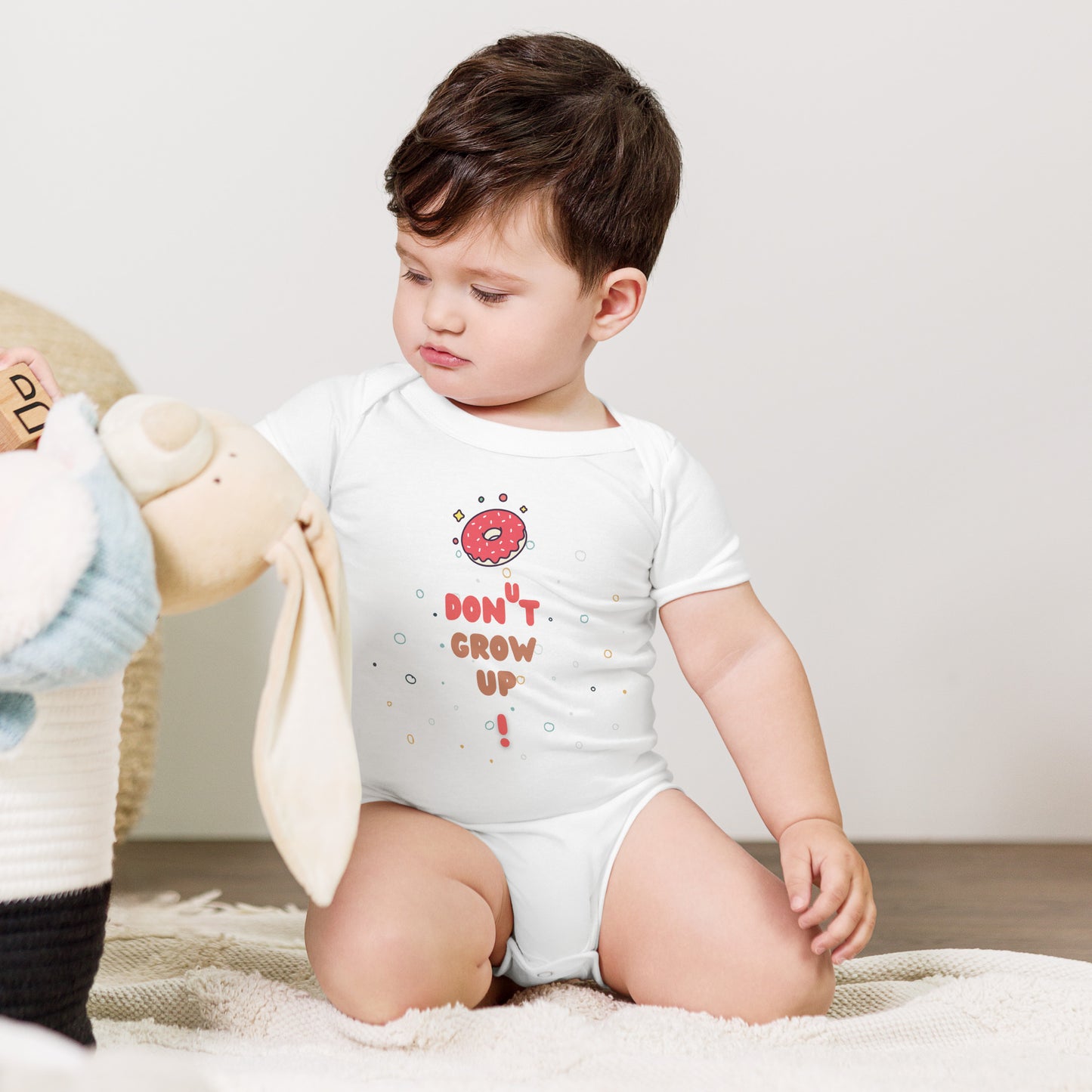 Baby in a white onesie with "Don't Grow Up!" with donut caption.