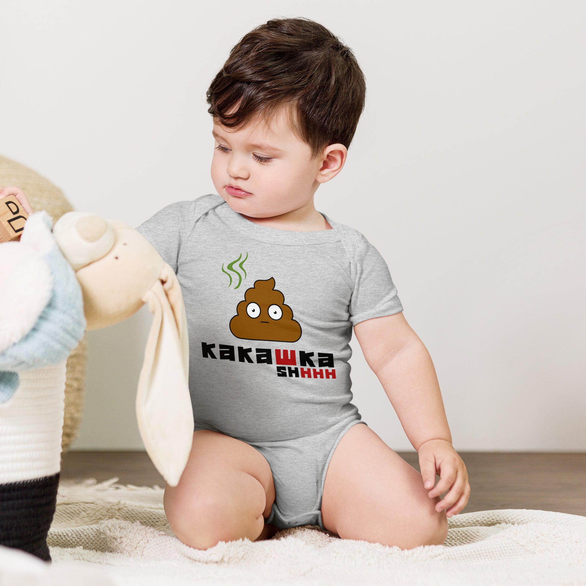 baby in grey one piece onesie with picture of poop and kakashka written on it