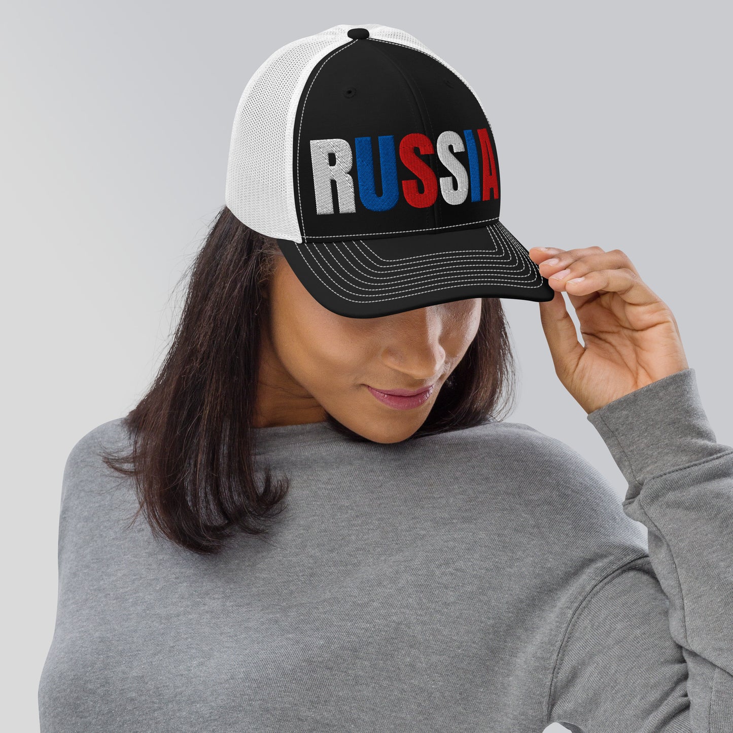 Woman wearing an embroidered 'RUSSIA' trucker hat with Russian flag colors. Classic design featuring a cotton blend front, mesh back, and adjustable snapback for a comfortable, stylish fit.